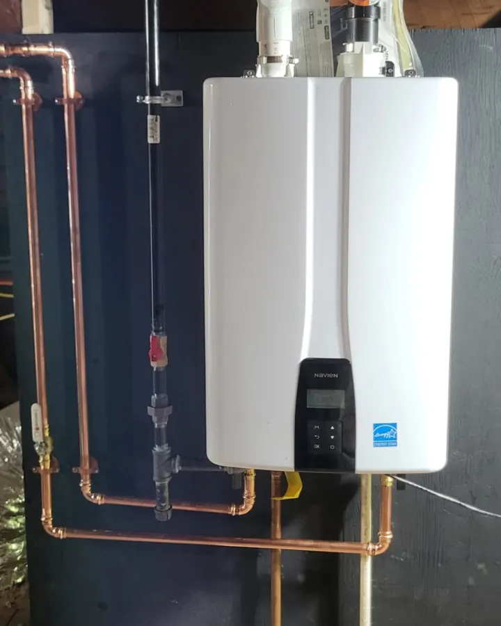 A Navien tankless water heater on a dark backer board, with copper supply loops and a red-handled gas shutoff