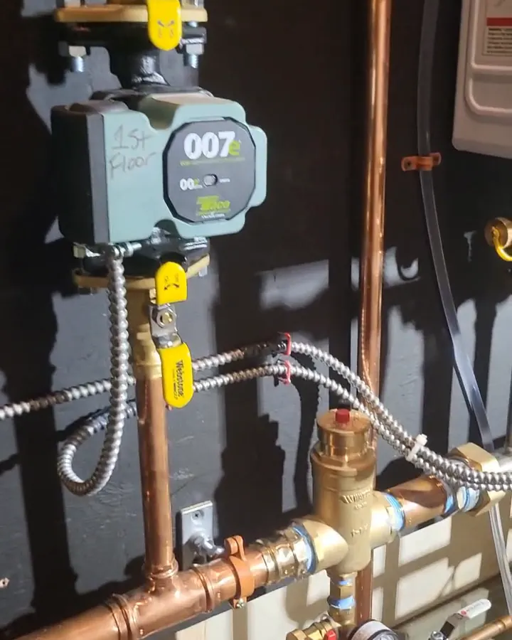 A circulator pump marked for its zone, above a brass air separator and pressure gauge on the copper supply