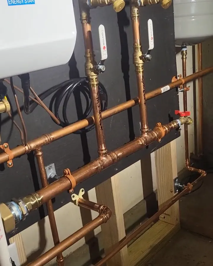 A copper heating manifold with red-handled drain valves, strapped square to a dark backer board