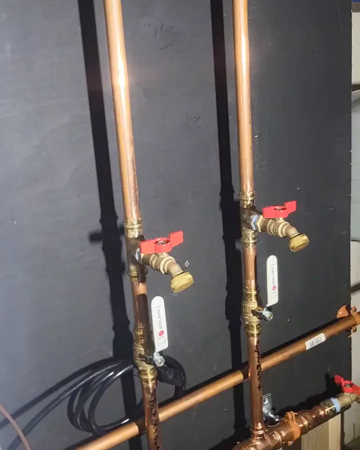 Two heating zones side by side, each with a red-handled drain and its zone name written on the pipe